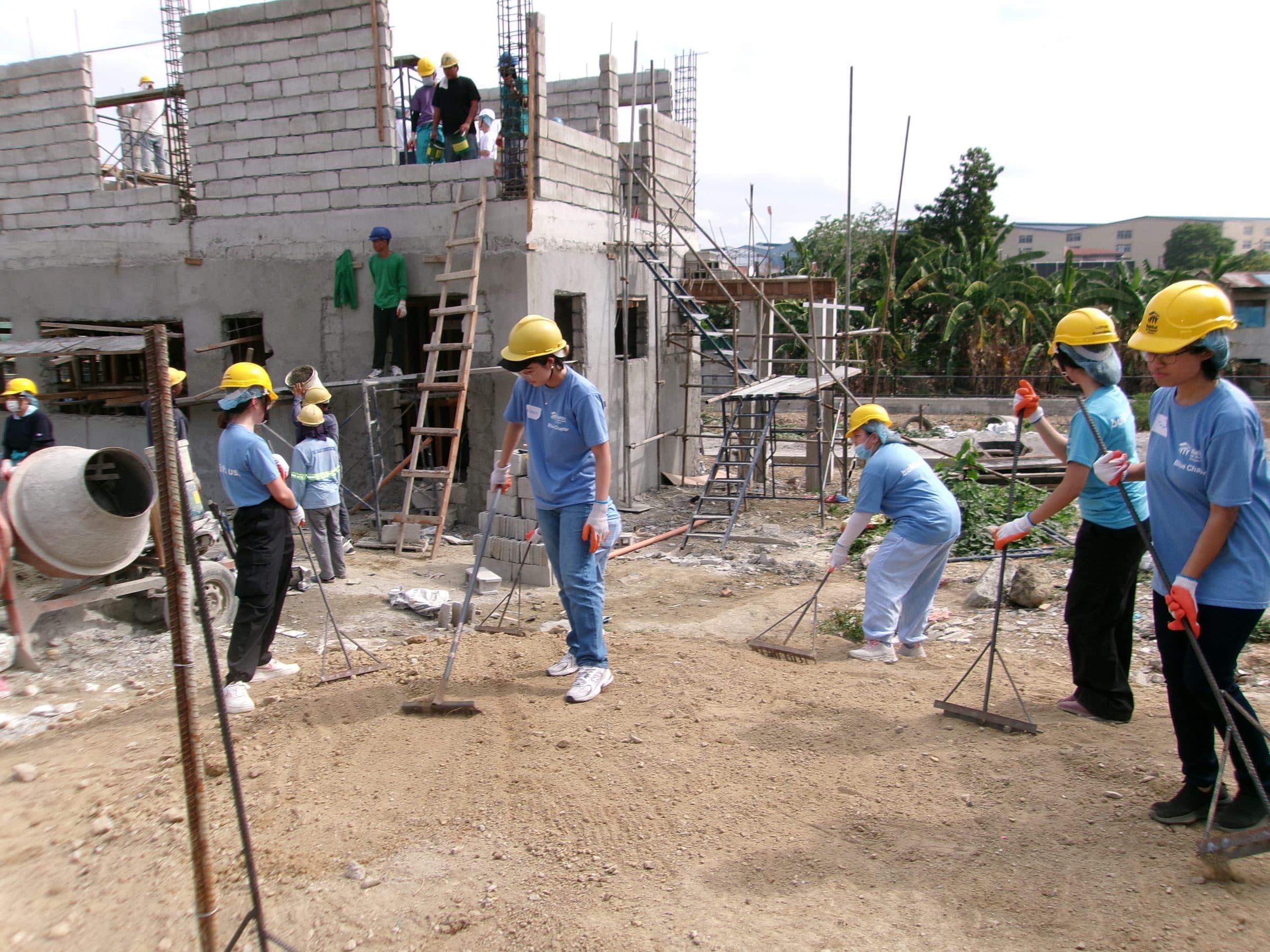 Members in hardhats raking gravel beside a half-built home