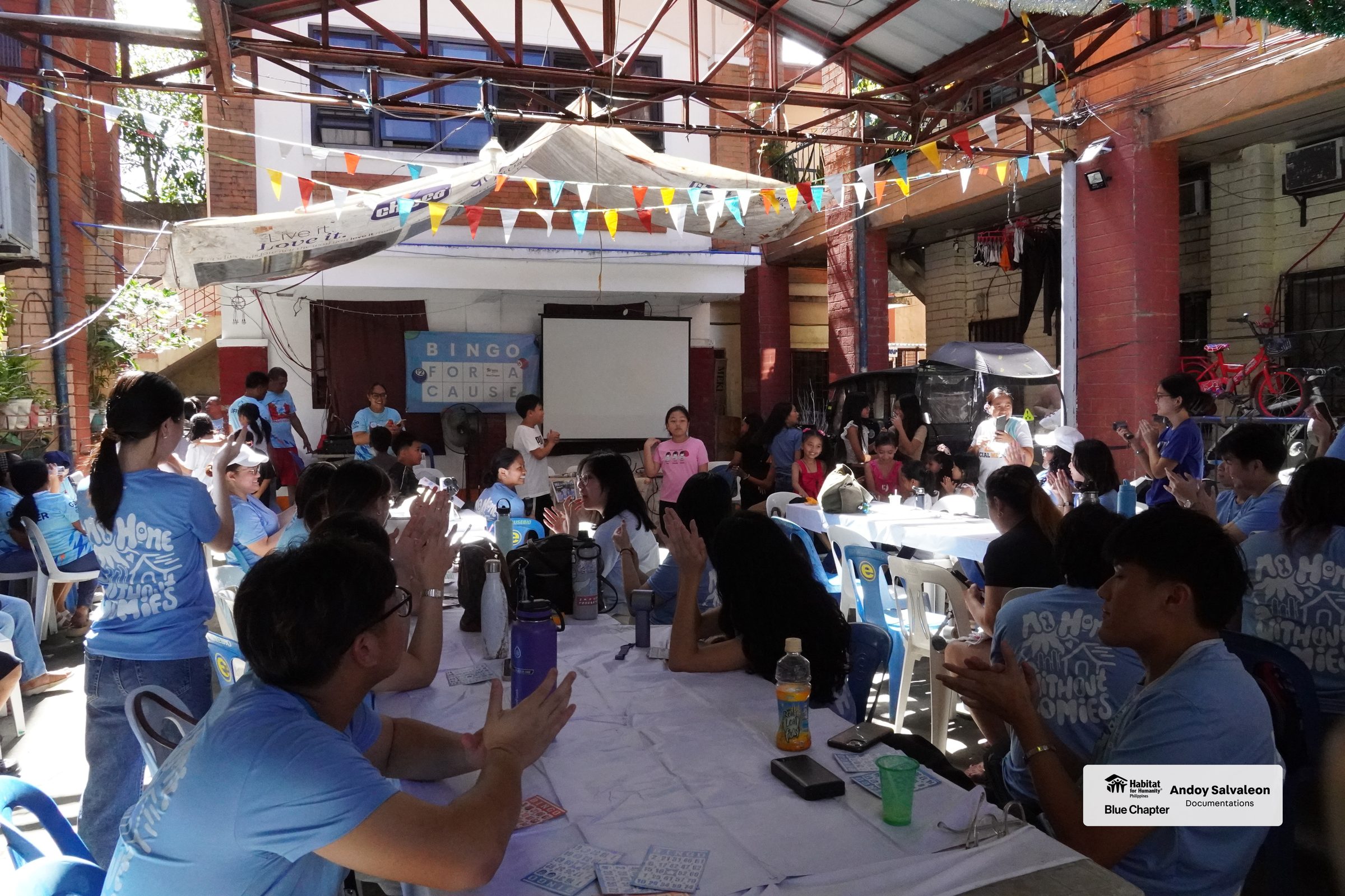 Members and residents playing bingo together under buntings in a community alley