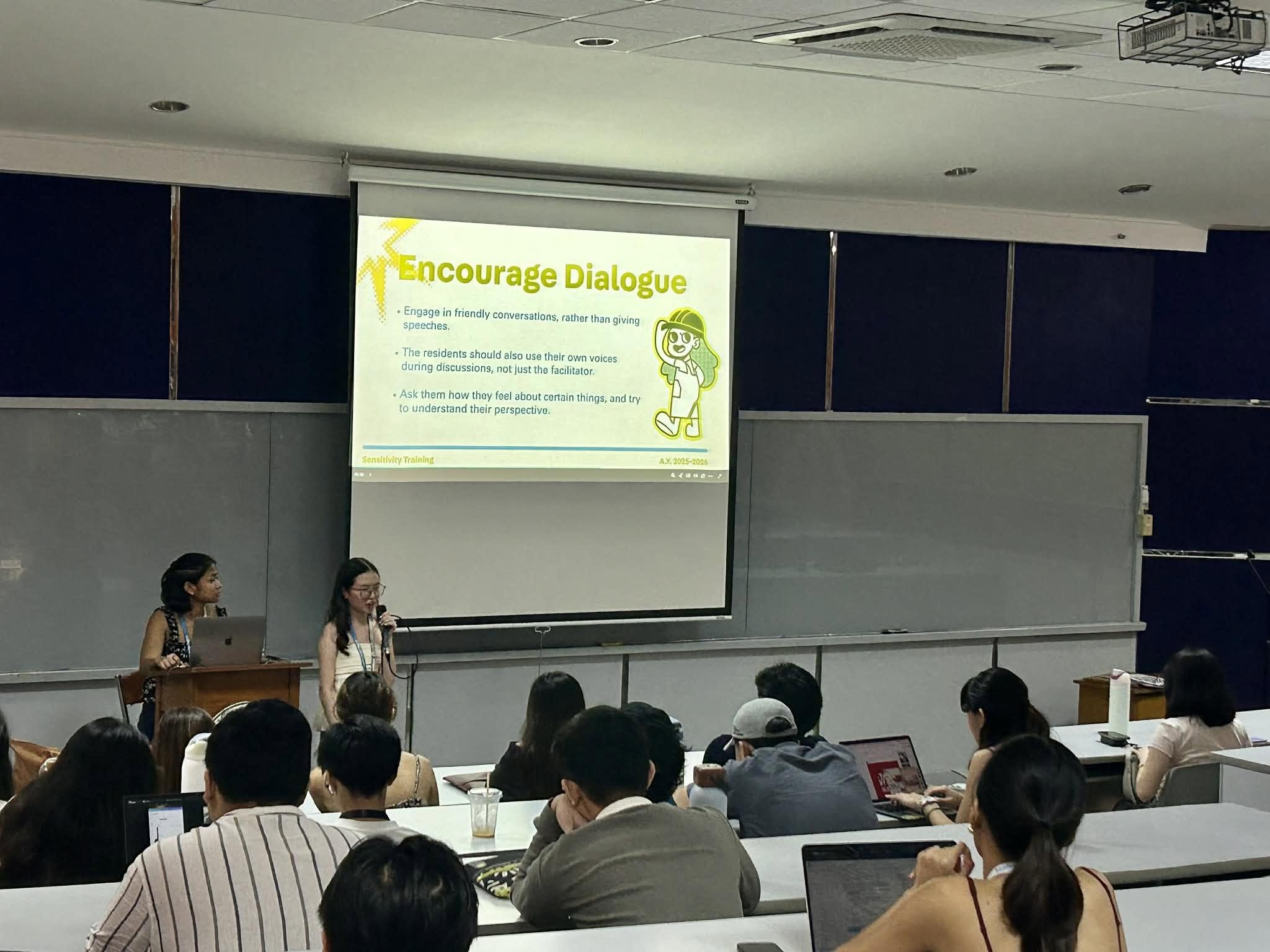 Two members leading a sensitivity training session, beside a slide reading “Encourage dialogue”